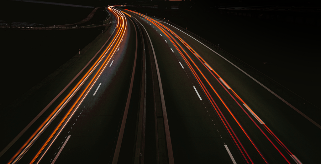 Luftaufnahme einer Autobahn bei Nacht mit langen Lichtspuren vorbeifahrender Fahrzeuge